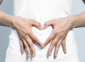 Woman making heart shape over tummy with hands