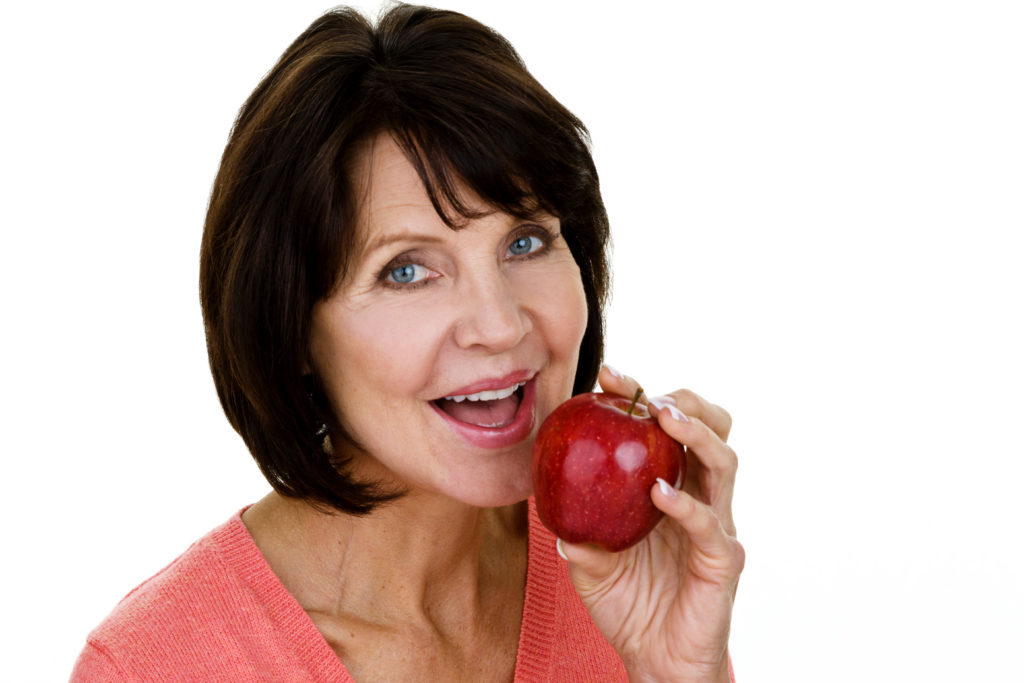 Beautiful mature woman eating an apple while being isolated on white background