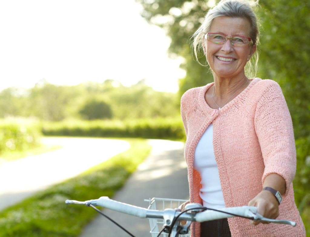 Smiling senior woman standing on a country lane with her bicycle