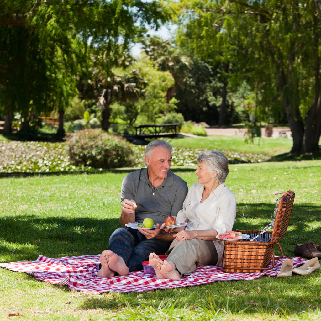 Mature couple enjoying picnic on a rug under trees in a park