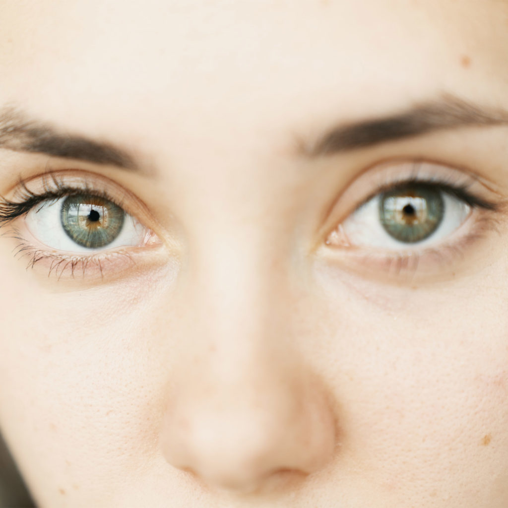 Close-up of young white woman's face, make-up free, green eyes, serious expression
