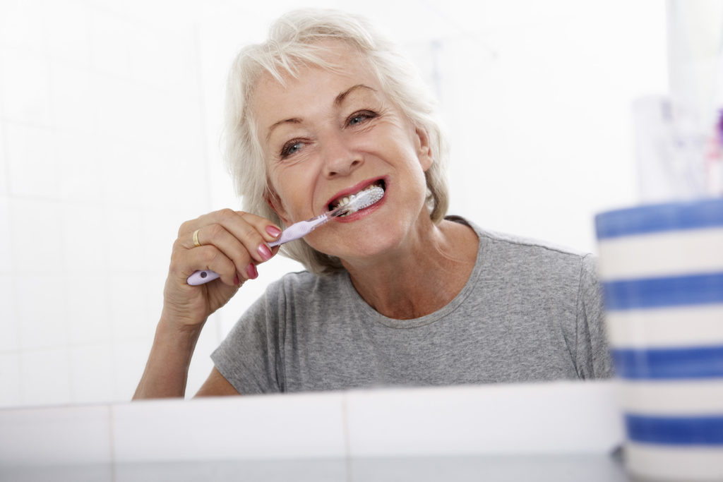 Senior Woman In Bathroom Brushing Teeth At Home