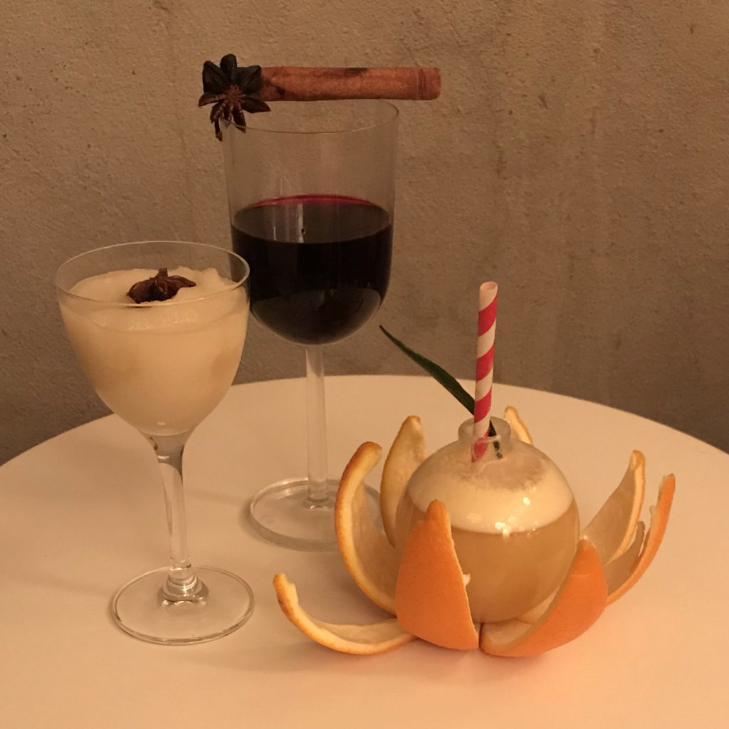 One glass of creamy apple, a glass of deep red mocktail garnished with a cinnamon stick, and a glass ball garnished with orange peel and a striped straw