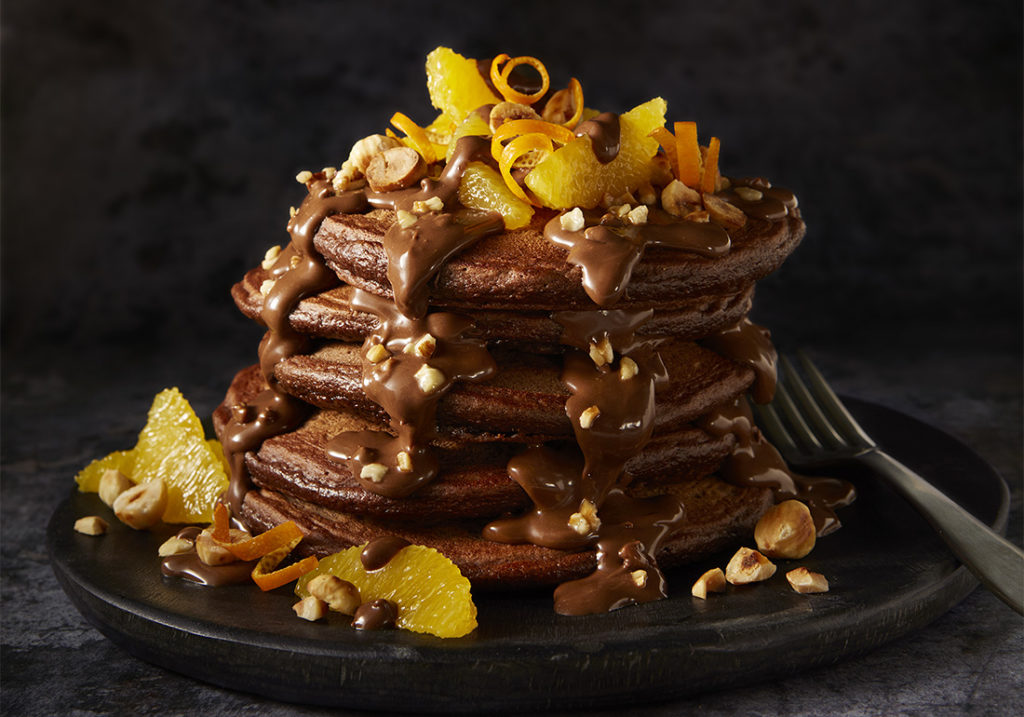 Shrove Tuesday Stack of chocolate pancakes, drizzled with chocolate sauce, hazelnuts and garnished with orange segments