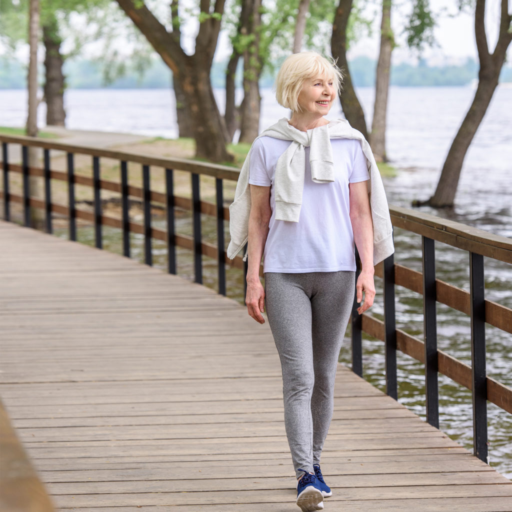 smiling senior woman walking on wooden boardwalk in park