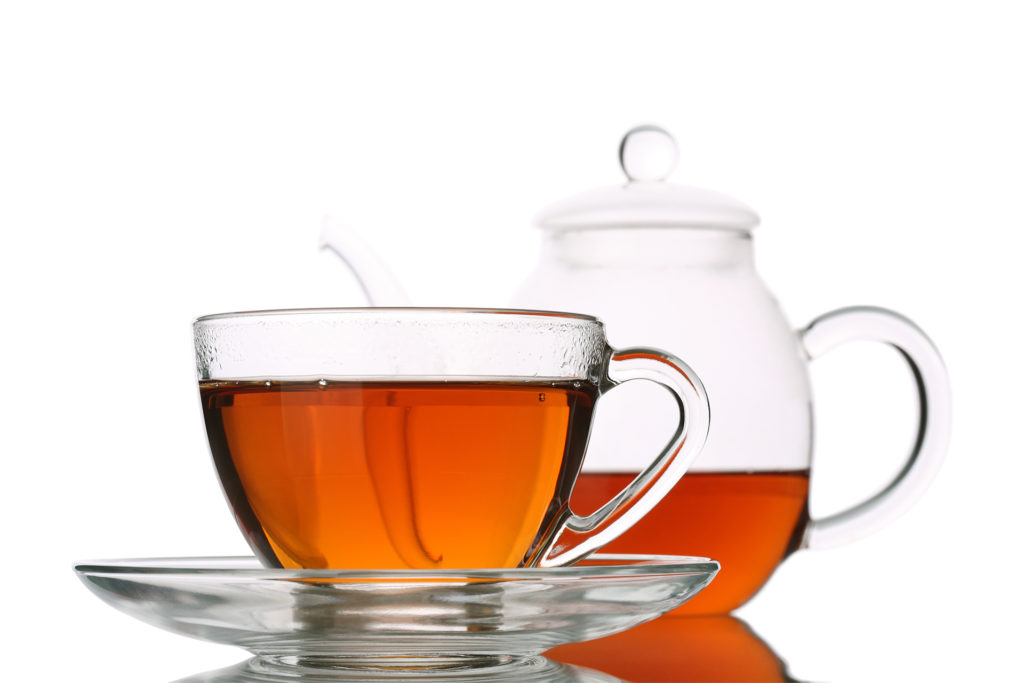 Glass cup of tea beside glass tea pot