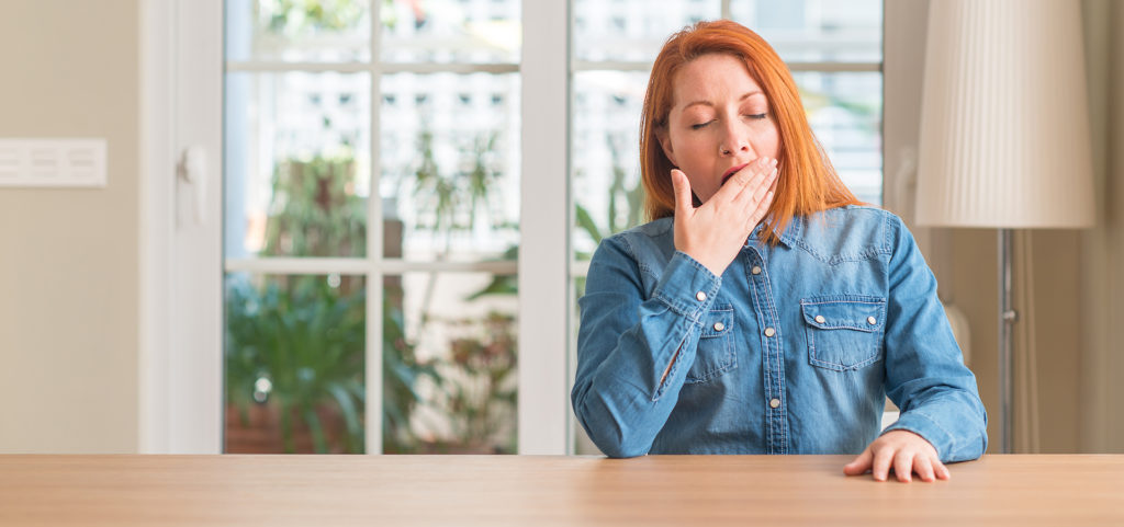 Redhead woman at home bored yawning tired covering mouth with hand. Restless and sleepiness.