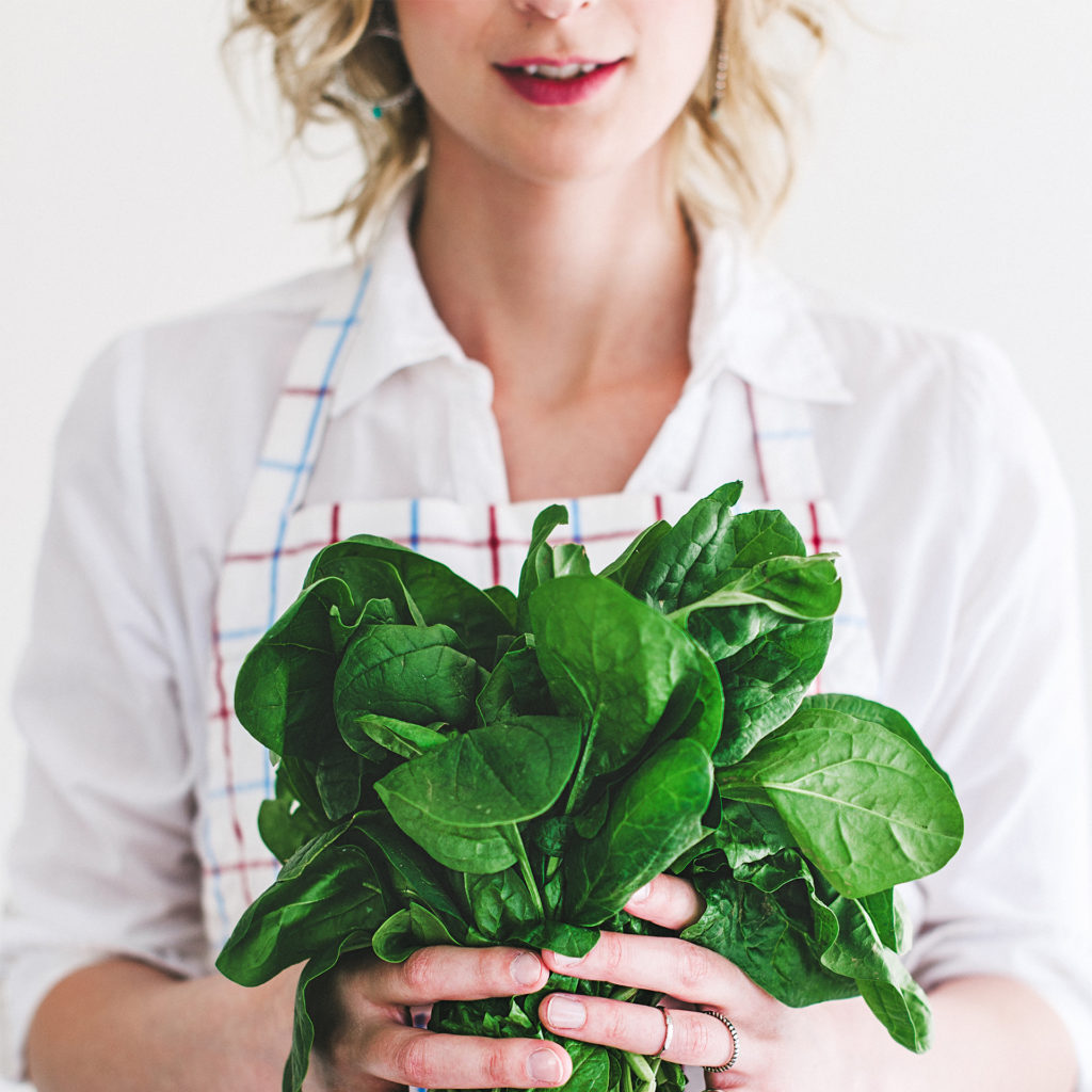 Young woman holding a bunch of fresh spinach stems in both hands against her stomach