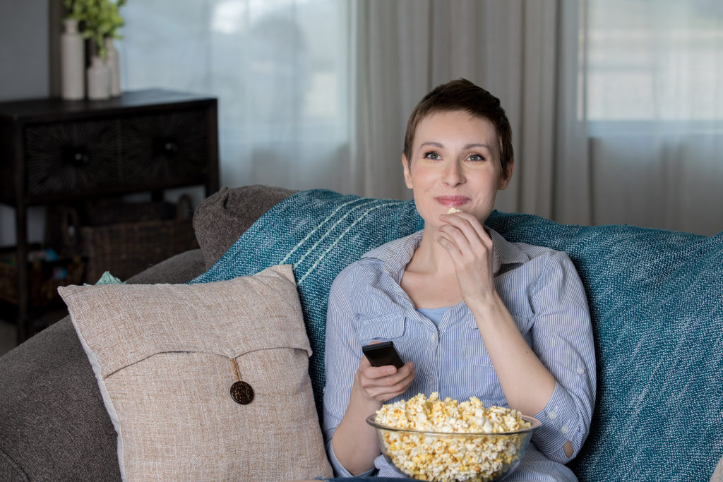 Happy mid adult woman eating popcorn while watching a movie at home in living room