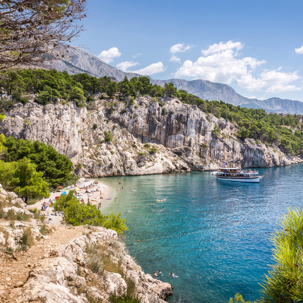 Small beach with steep white cliffs, turquoise water and tourist sight seeing boat