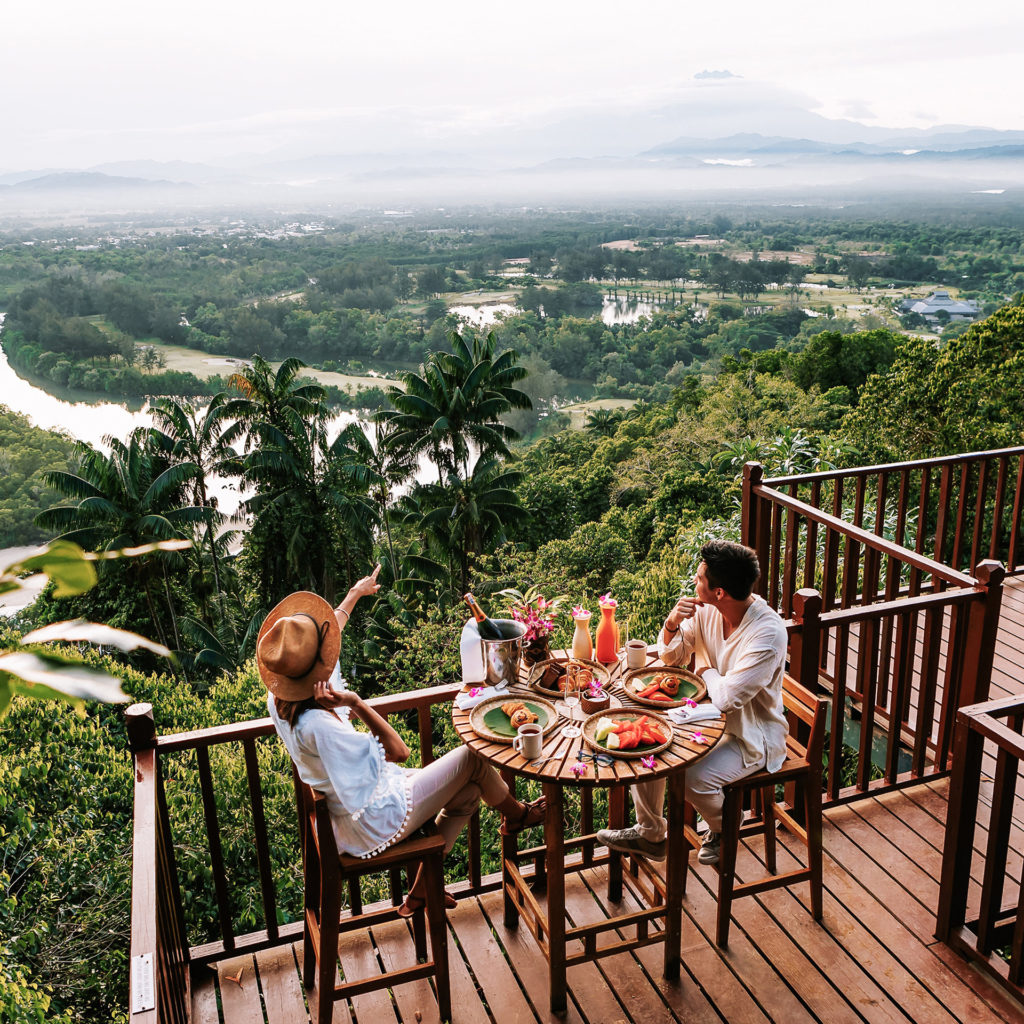 Couple enjoying breakfast on decking looking out over tropical rainforest and river below