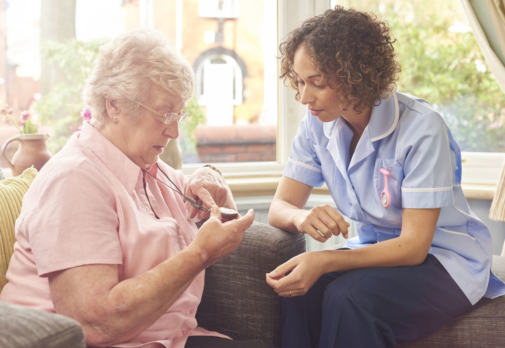 a care nurse demonstrates to a senior woman how her panic pendant would work in the event of a fall or medical emergency.
