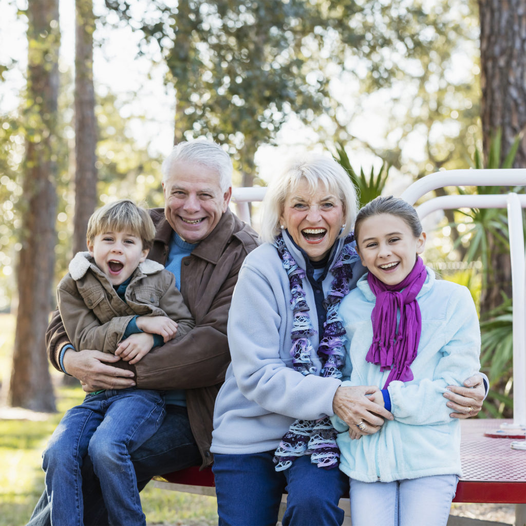 Elderly couple and two children aged 8-10 pose smiling in a rural play park
