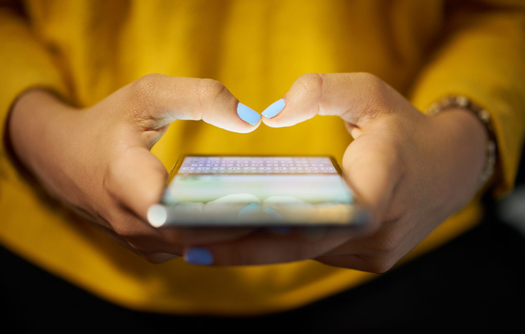 Woman in yellow jumper, pale blue nail varnish, typing social media post