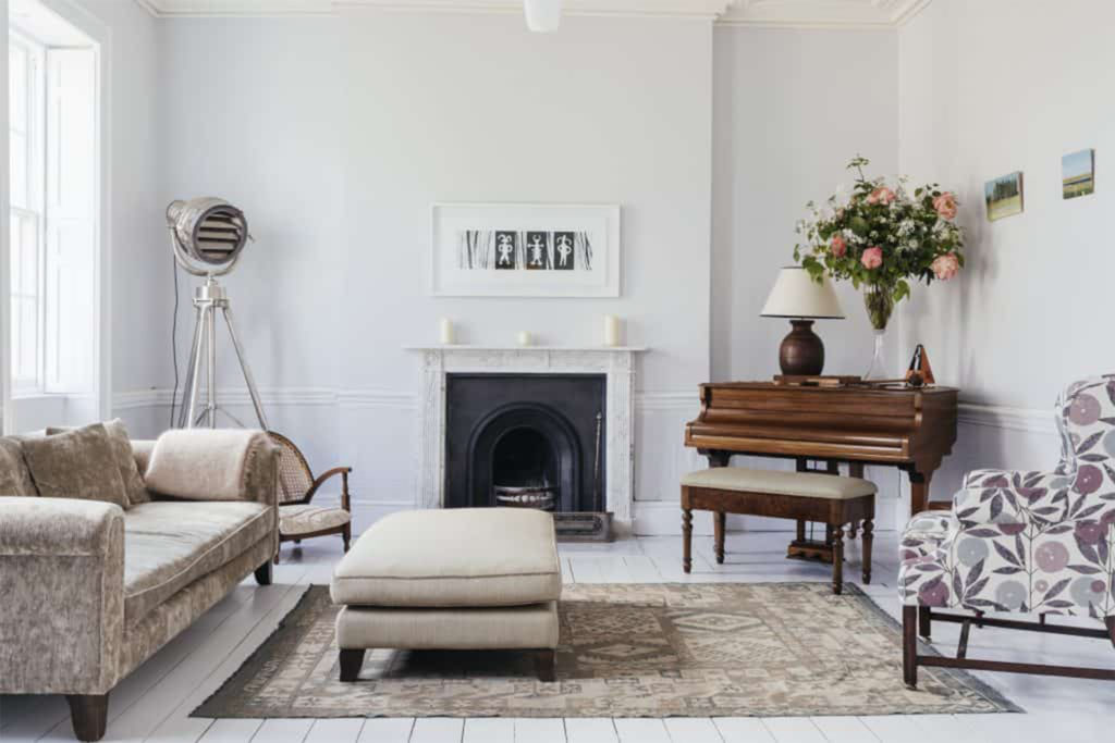Simply decorated white room with black period fireplace, neutral sofas and piano, plus contemporary fan/heater/light in the corner