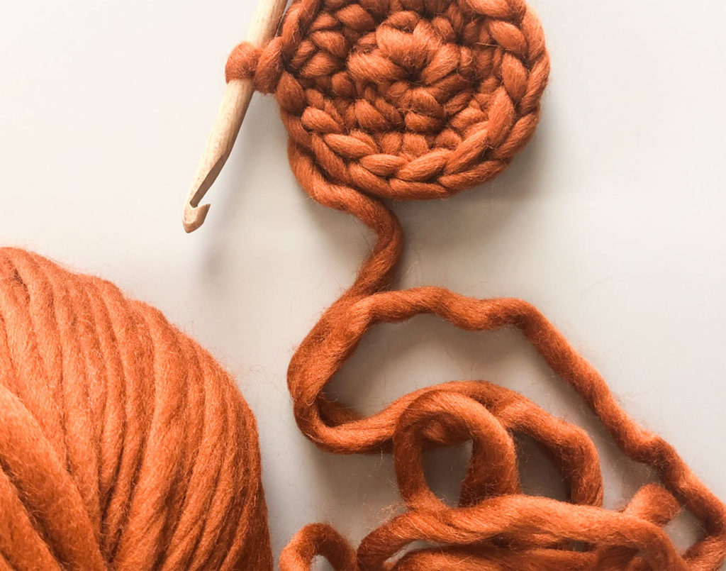 Small circle of crochet with wooden hook and burnt orange yarn