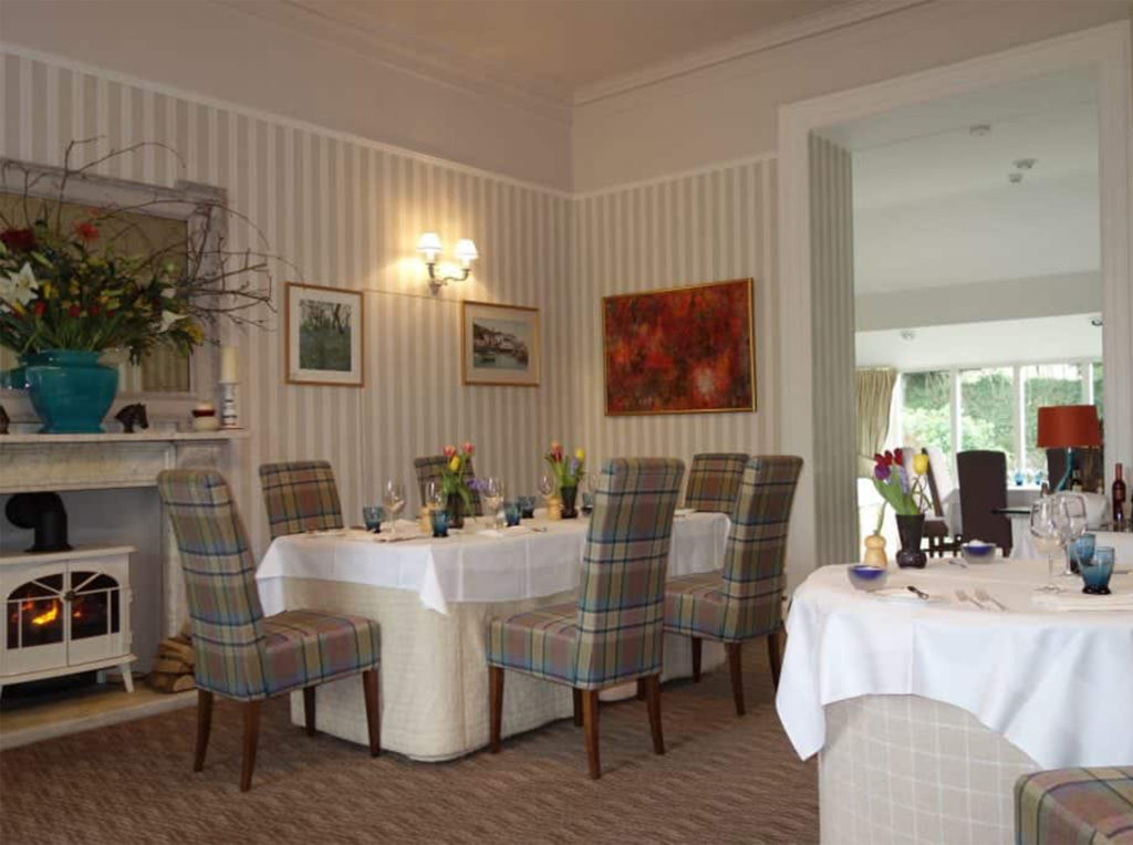 Cosy hotel dining room, neutral theme, with tartan upholstered chairs and wood burning stove