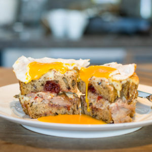 Toasted sandwich with turkey and cranberry, topped with soft fried egg, yolk dripping