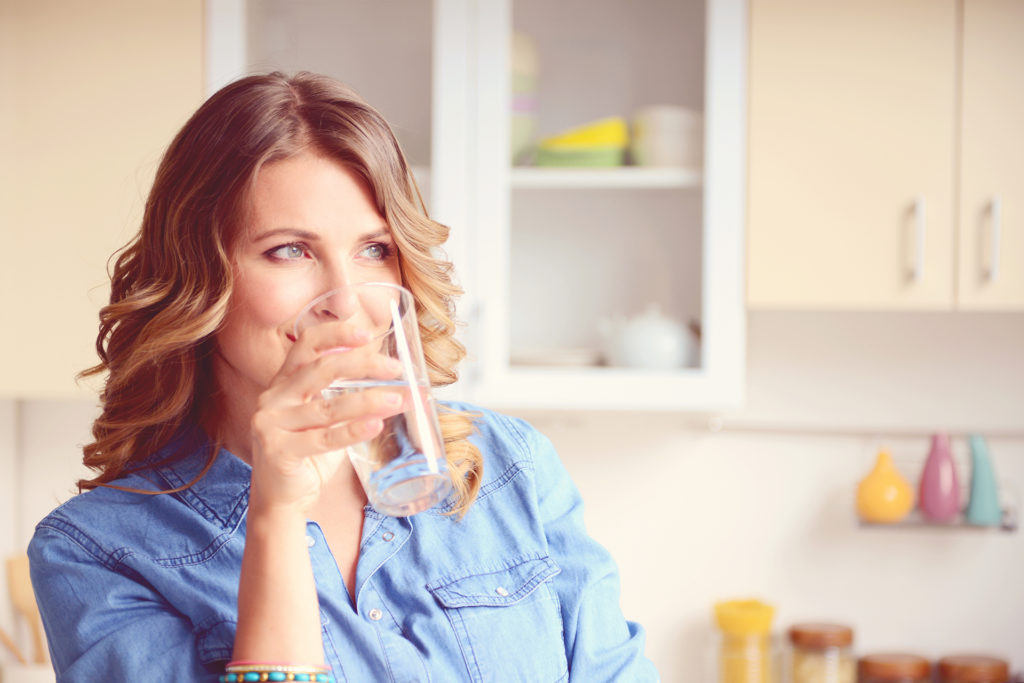 Blonce woman drinking glass of water in kitchen