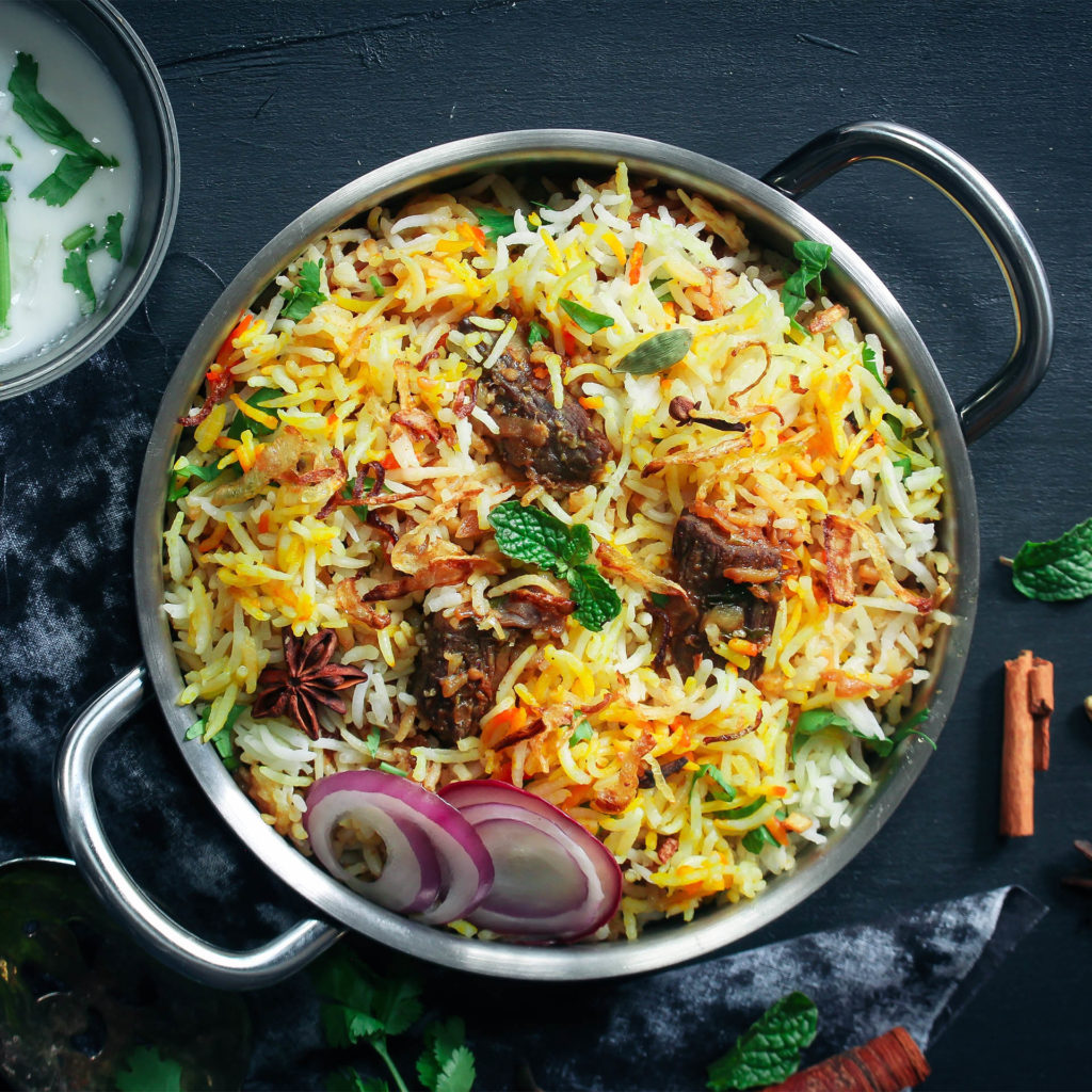Big pot of colourful rice biryani with fresh coriander, star anise and slices of raw red onion