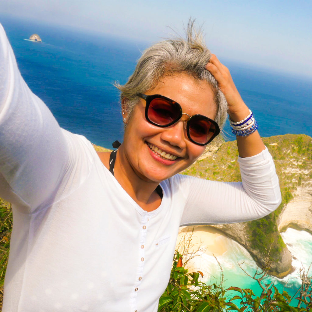 Woman taking holiday selfie, dangerously close to a cliff edge, sea and rocks can be seen below her