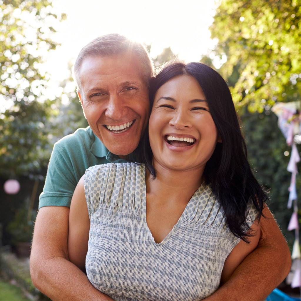 Man hugging woman from behind, in garden, both laughing
