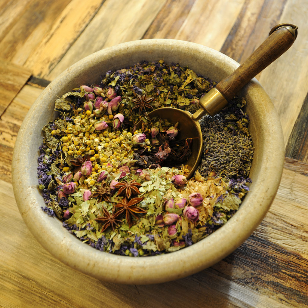 Beautiful bowl of dried herbs including rosebuds and chamomile heads, in a bowl with an ornate spoon