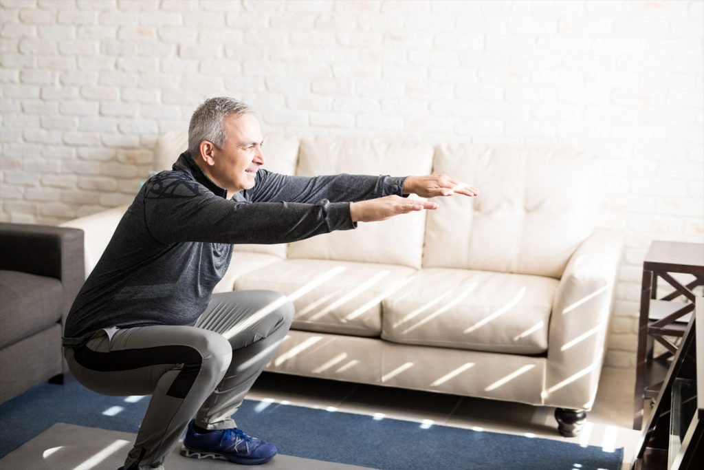Senior man doing squats and exercising in living room at home
