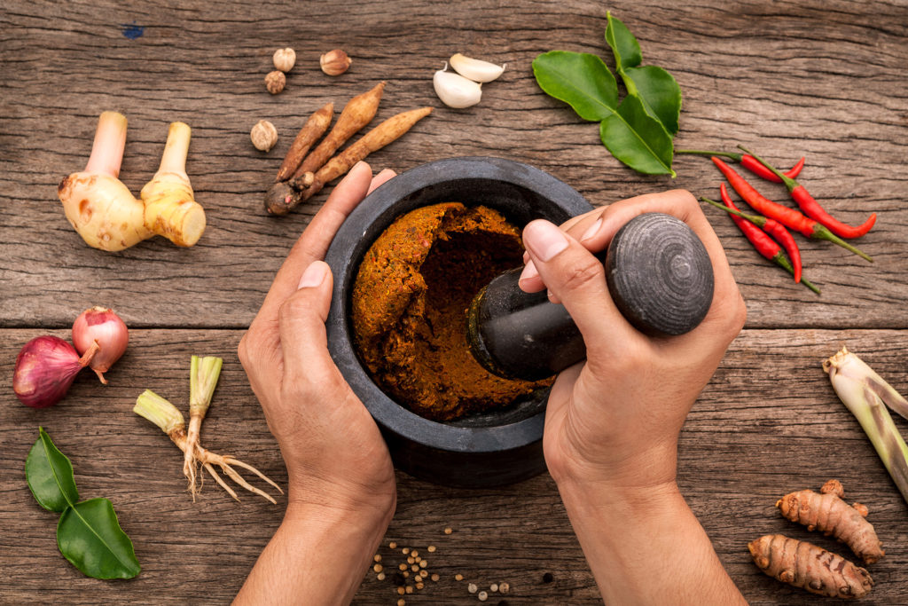 The Women hold pestle with mortar and spice paste of thai popular food red curry on rustic wooden background. Spices ingredients chilli ,pepper, garlic,galanga lemongrass and Kaffir lime leaves 
