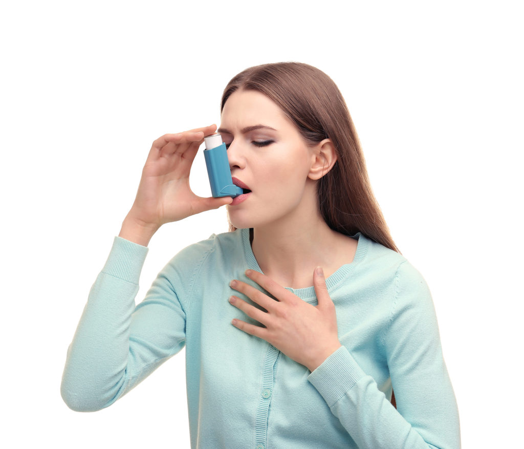 Young woman using asthma inhaler on white background;