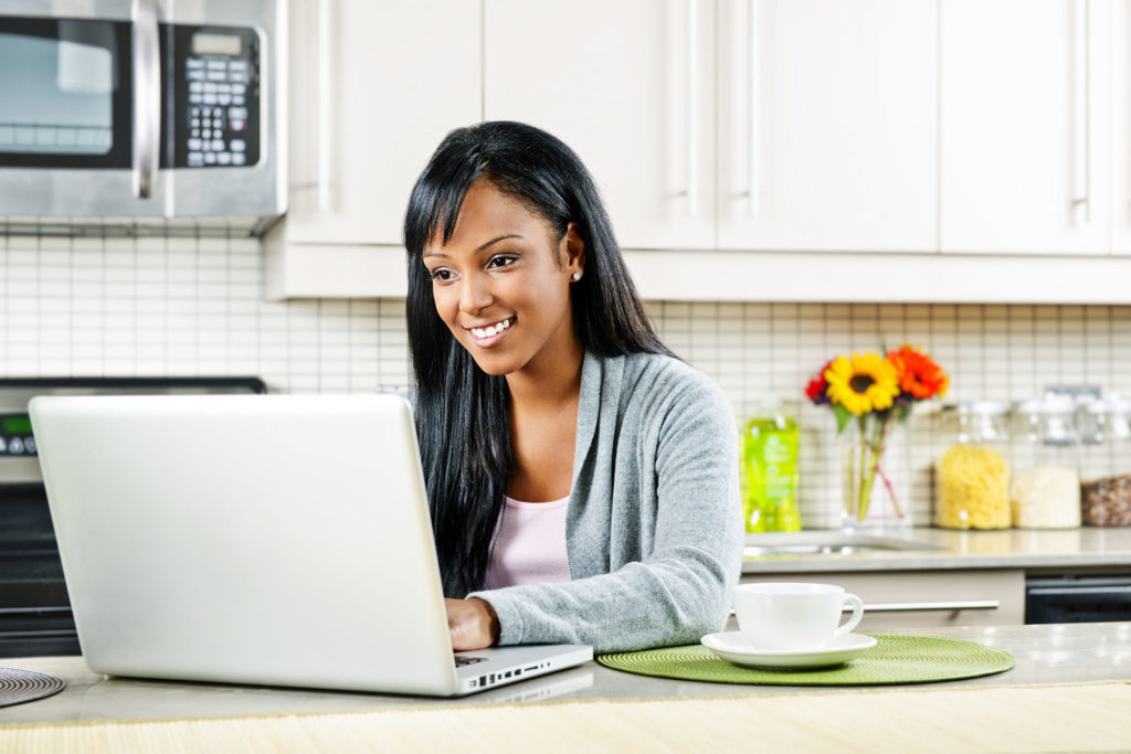 Smiling black woman using computer in modern kitchen interior; 