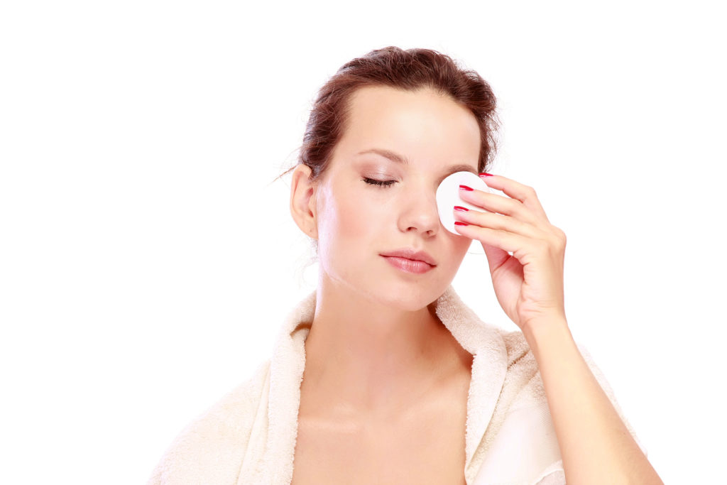 Young women wiping cotton wool pad over eyelid