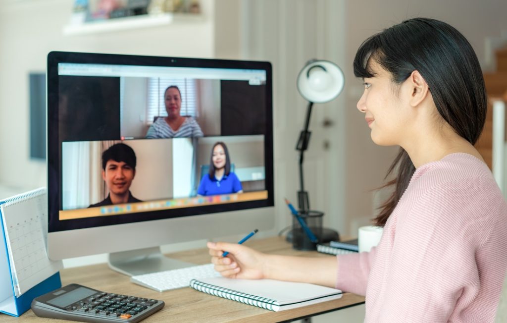 Woman looking at computer screen, video call with 3 other people who appear on the screen