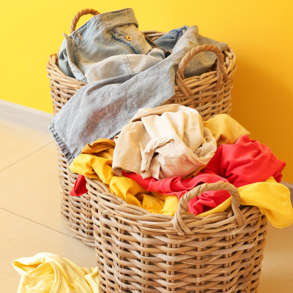 2 wicker laundry baskets full of discarded clothes, yellow wall behind