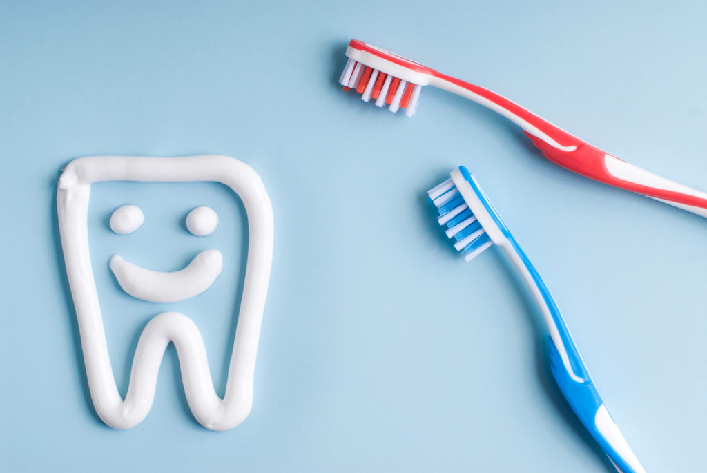 Toothpaste in a form of a smiling tooth. Red and blue toothbrushes. Toothpaste on blue. Dental hygiene.;