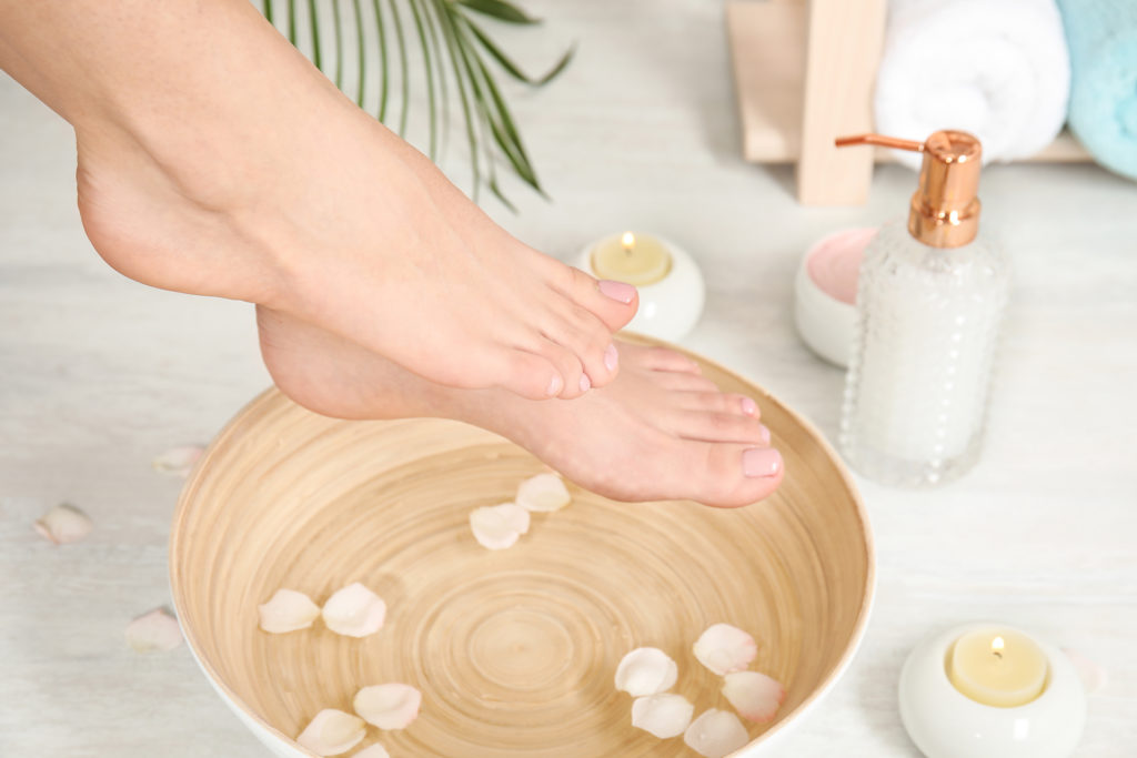 Woman putting her feet into bowl with water and rose petals indoors, closeup. Spa treatment; 