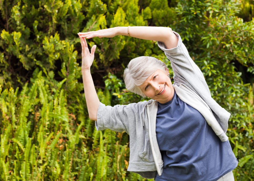 Mature woman doing her stretches in the garden; 
