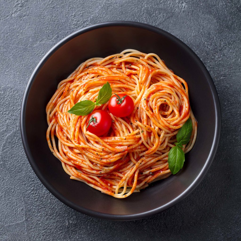 Pasta, spaghetti with tomato sauce in black bowl. Grey stone background. Top view. Close up.
