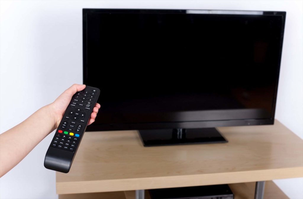 Hand turning off on the television with a remote control