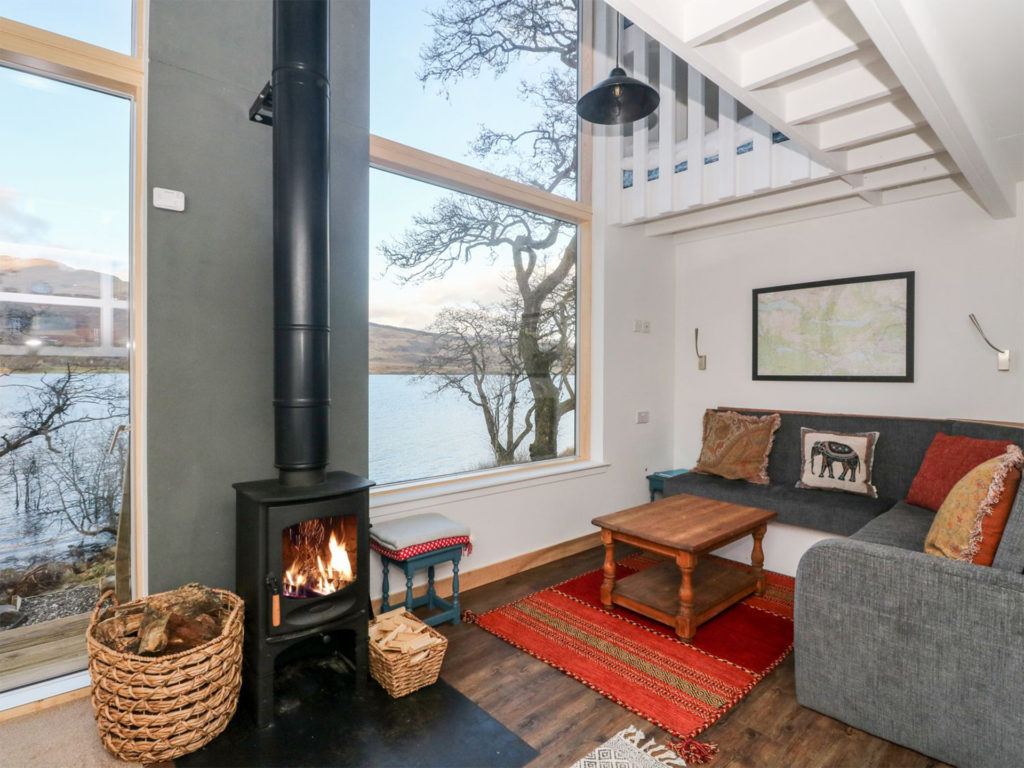 Modern log cabin with huge window and small woodburning stove with long pipe, red rug and tasteful sofas