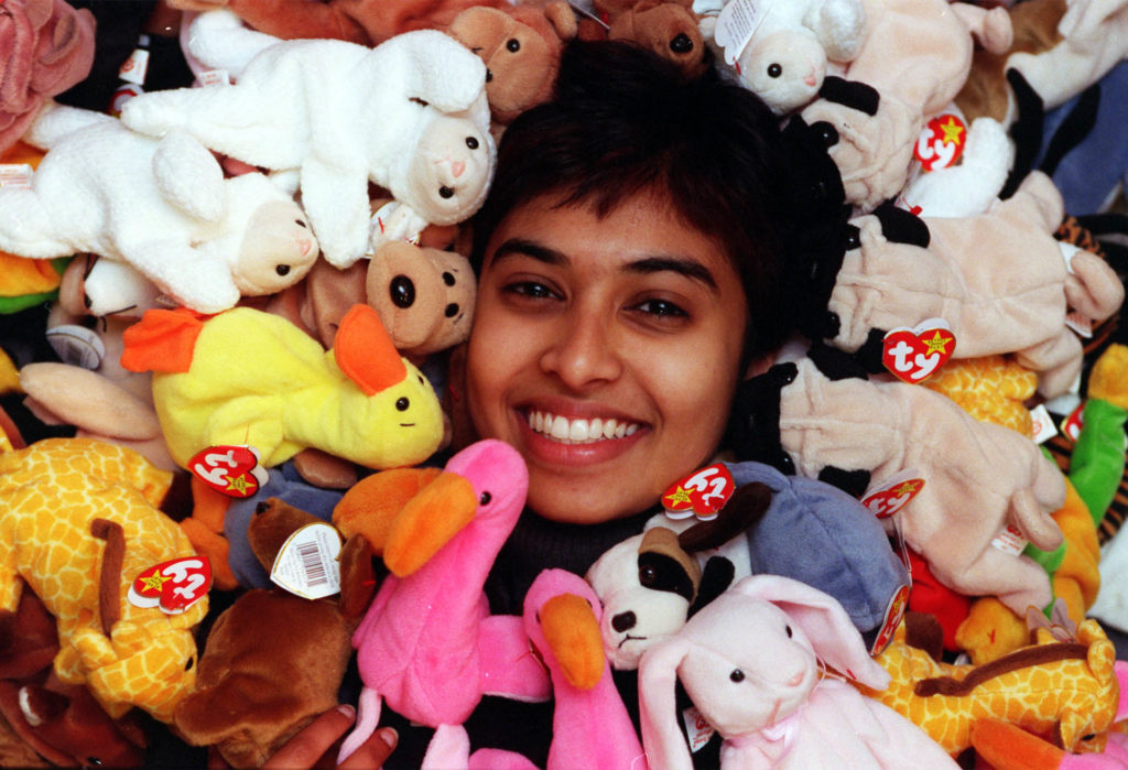 Young woman laughing, her face surrounded by Beanie Babies soft toys including a bright pink flamingo and yellow duck