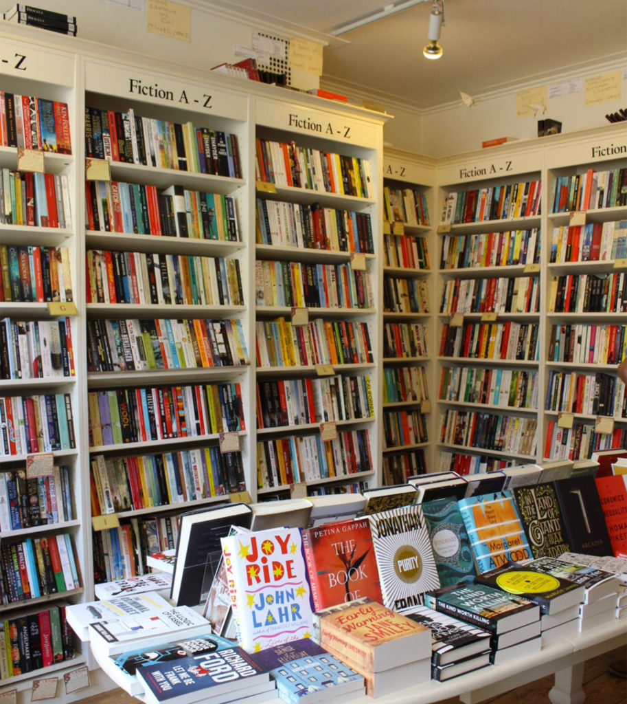 Interior of Mr B's Emporium, bright modern bookshop with tall white shelves and more books on a table