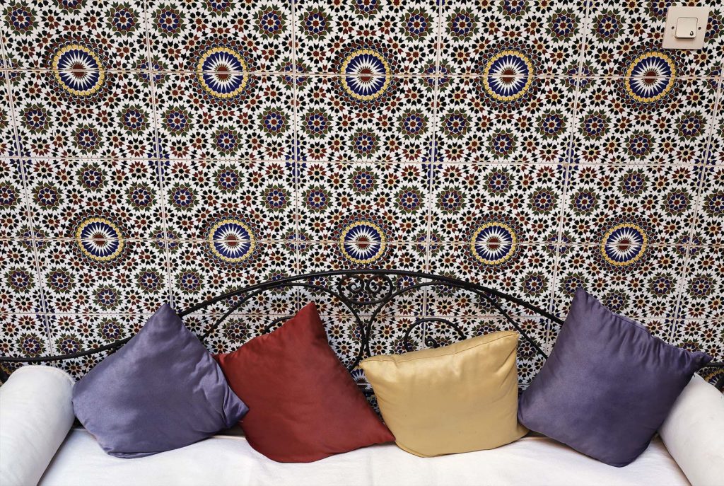 Sofa with coloured cushions in front o a tiled wall, patio of a Riad, Marrakech, Morocco, Africa