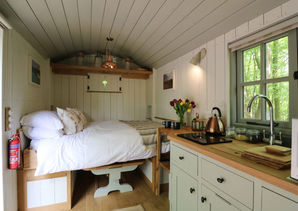 Interior of shepherd's hut, kitchen in middle and cosy double bed pulled out over table at one end