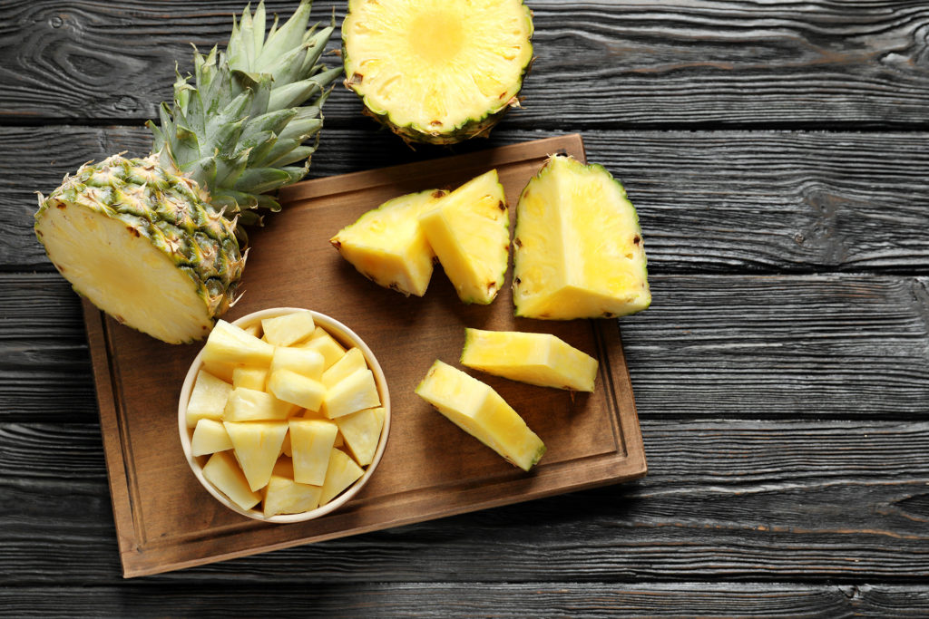 Wooden board with fresh sliced pineapple on table, top view; 