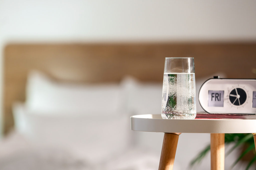 Glass of water and alarm clock on table in bedroom; 