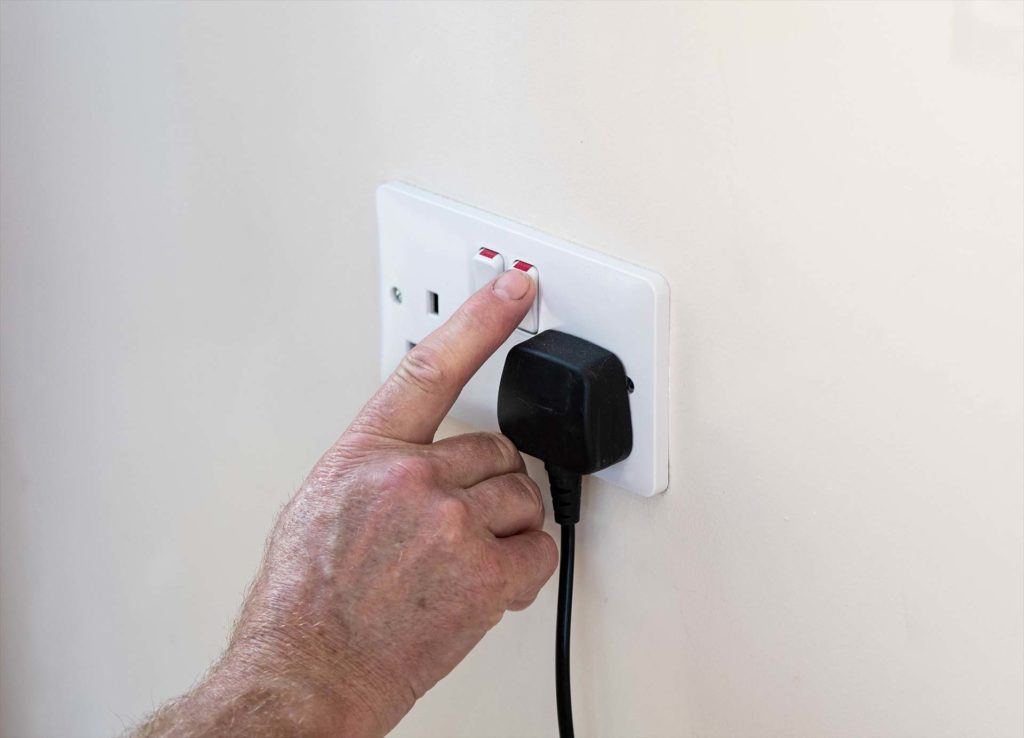 Mans hand turning off plug socket to save electricity and the planet