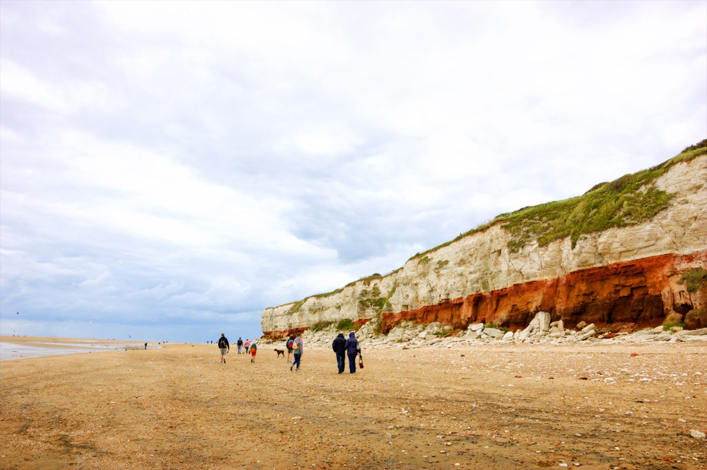 People walking Hunstanton cliffs beach. These famous red and white striped cliffs at Norfolk, UK are popular tourist attraction.