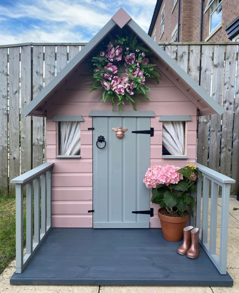 Cute wooden playhouse with banisters and wreath over door, painted in pink and grey
