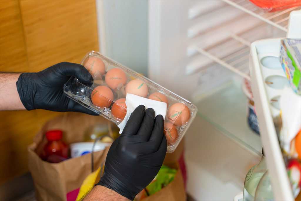 COVID-19: Is it necessary to clean your groceries delivered at home? Man in quarantine wiping plastic package with sanitizing wipes after shopping or receiving online delivery bags.